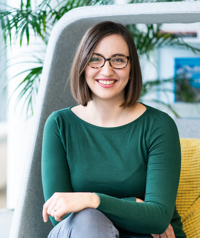 The photo of Paulina Sedlak-Jakubowska. A caucasian woman in her 30's, with shoulder length brown hair and big glasses. Wearing a green longsleeve. Sitting inside an office space.